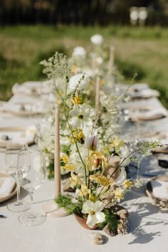 a long table with white and yellow flowers in vases on it, surrounded by candles