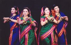 three women dressed in colorful sari and holding hands up to their chests, both wearing