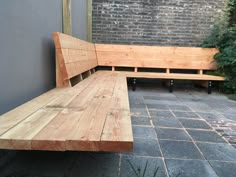 a wooden bench sitting on top of a stone walkway next to a brick wall and green bushes