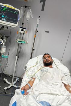 a man laying in a hospital bed with an iv and monitors on the wall behind him