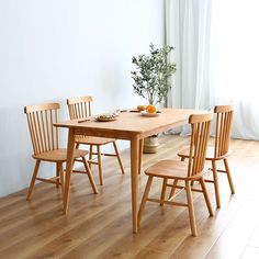 a wooden table and four chairs in a room with white walls, hardwood flooring and windows