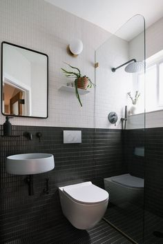 a white toilet sitting next to a bathroom sink under a mirror on top of a tiled wall