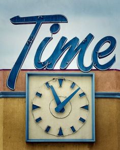 a clock on the side of a building that says time and has blue letters above it