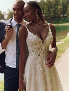 a man and woman standing next to each other in front of a lake wearing wedding dresses