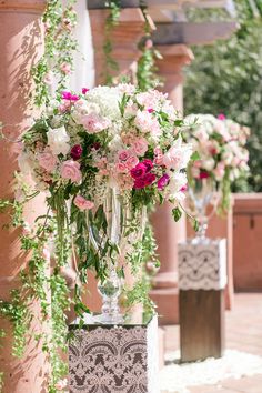 tall vases filled with pink and white flowers on top of a stone block wall