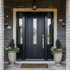 a black front door with two planters on either side and a welcome mat in the middle