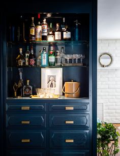 an open cabinet with liquor bottles and glasses on the top, next to a potted plant