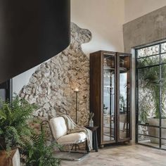 a living room filled with furniture next to a stone wall covered in plants and potted plants