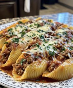 a white plate topped with stuffed shells covered in sauce and ground meat, on top of a patterned table cloth