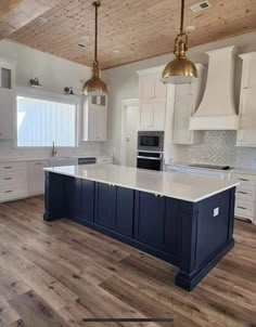 a large kitchen with white cabinets and blue island counter tops, gold pendant lights over the sink