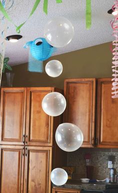 balloons and streamers are hanging from the ceiling above a kitchen counter with wooden cabinets