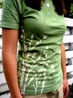 a woman standing in front of a white fence wearing a green t - shirt with flowers on it