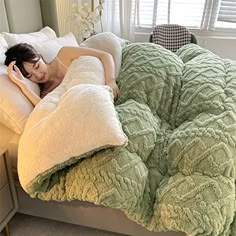 a woman laying in bed on top of a green comforter