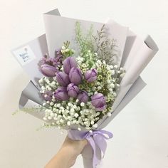 a hand holding a bouquet of purple tulips and baby's breath flowers