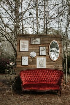 a red couch sitting in front of a wooden wall with pictures on it's side