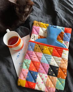 a cat sitting next to a quilted placemat and cup of tea on a bed