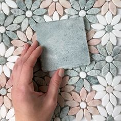 a hand holding a piece of tile on top of a flowered surface with white and gray pebbles