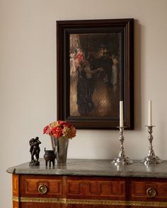 a painting is hanging on the wall above a table with candles and figurines