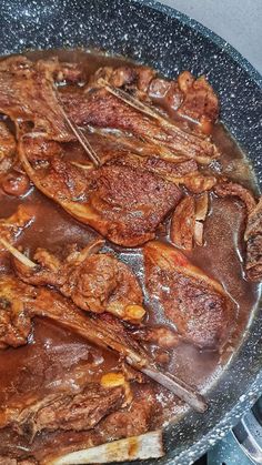 some meat is being cooked in a skillet on the stove top with tongs