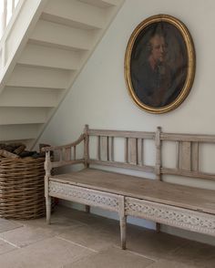 a painting hangs on the wall next to a wooden bench and wicker basket in front of it