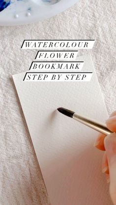 a person is writing on paper with a pen and watercolor flower in the background