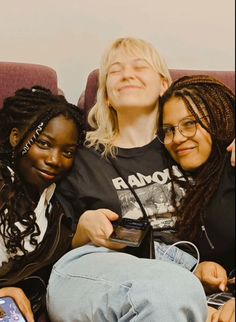 three young women sitting on a couch looking at their cell phones and smiling for the camera