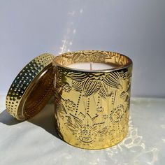 a gold colored candle is sitting on a white surface with an intricately designed lid