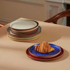 a blue plate topped with a croissant on top of a table next to plates