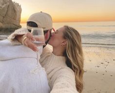 a man and woman kissing on the beach with a glass of wine in front of them