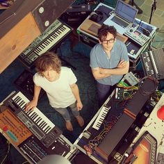 two young men standing in front of electronic equipment, looking down at the camera man