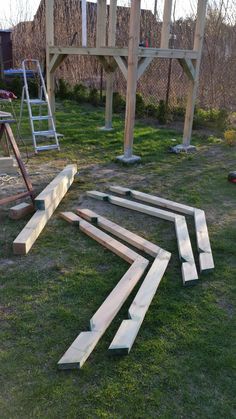 several pieces of wood are laying on the grass in front of a wooden structure with ladders