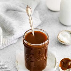 a spoon in a jar filled with caramel sauce on top of a white plate