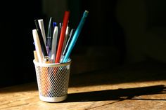 a cup filled with lots of different colored pens