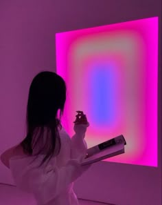 a woman holding a book in front of a pink and blue light filled room with square shapes