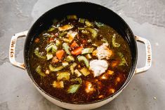 a pot filled with soup and vegetables on top of a cement floor next to a wooden spoon