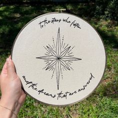 a person holding up a hand embroidered star ornament with writing on it in the grass