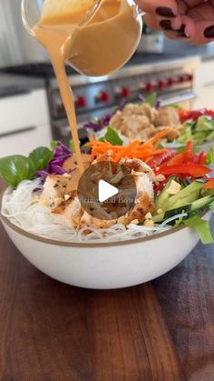 someone pouring dressing over a salad in a bowl