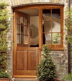 a wooden door is open in front of a brick building with potted plants on the side