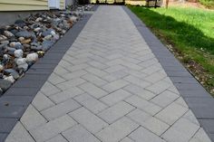 a brick walkway in front of a house with rocks and grass on the side walk