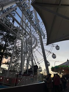 the ferris wheel at an amusement park with people standing around and watching it go by