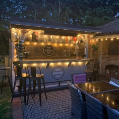 an outdoor bar is lit up at night with string lights on the roof and chairs around it