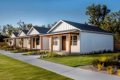 a row of small white houses sitting on top of a lush green field next to trees