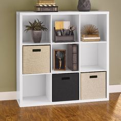 a white bookcase with four different baskets on top and two plants in the middle