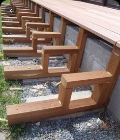 several wooden benches sitting next to each other on the side of a building with gravel and grass