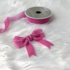 a roll of pink satin ribbon with a bow on the end, sitting on white fur