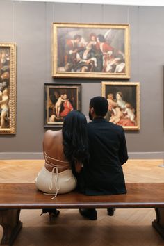 a man and woman sitting on a bench in front of some art work with paintings behind them