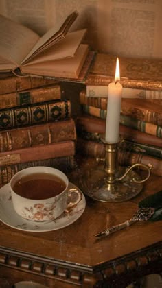 a cup of tea sits on a table next to some books and a lit candle