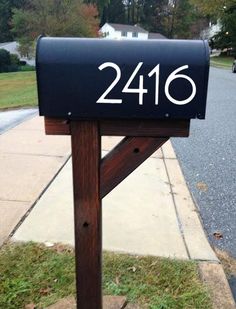 a black mailbox sitting on the side of a road next to a street with houses in the background