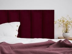 a white bed topped with pillows and a red headboard next to a vase filled with flowers