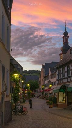 a person walking down a cobblestone street at dusk with buildings in the background